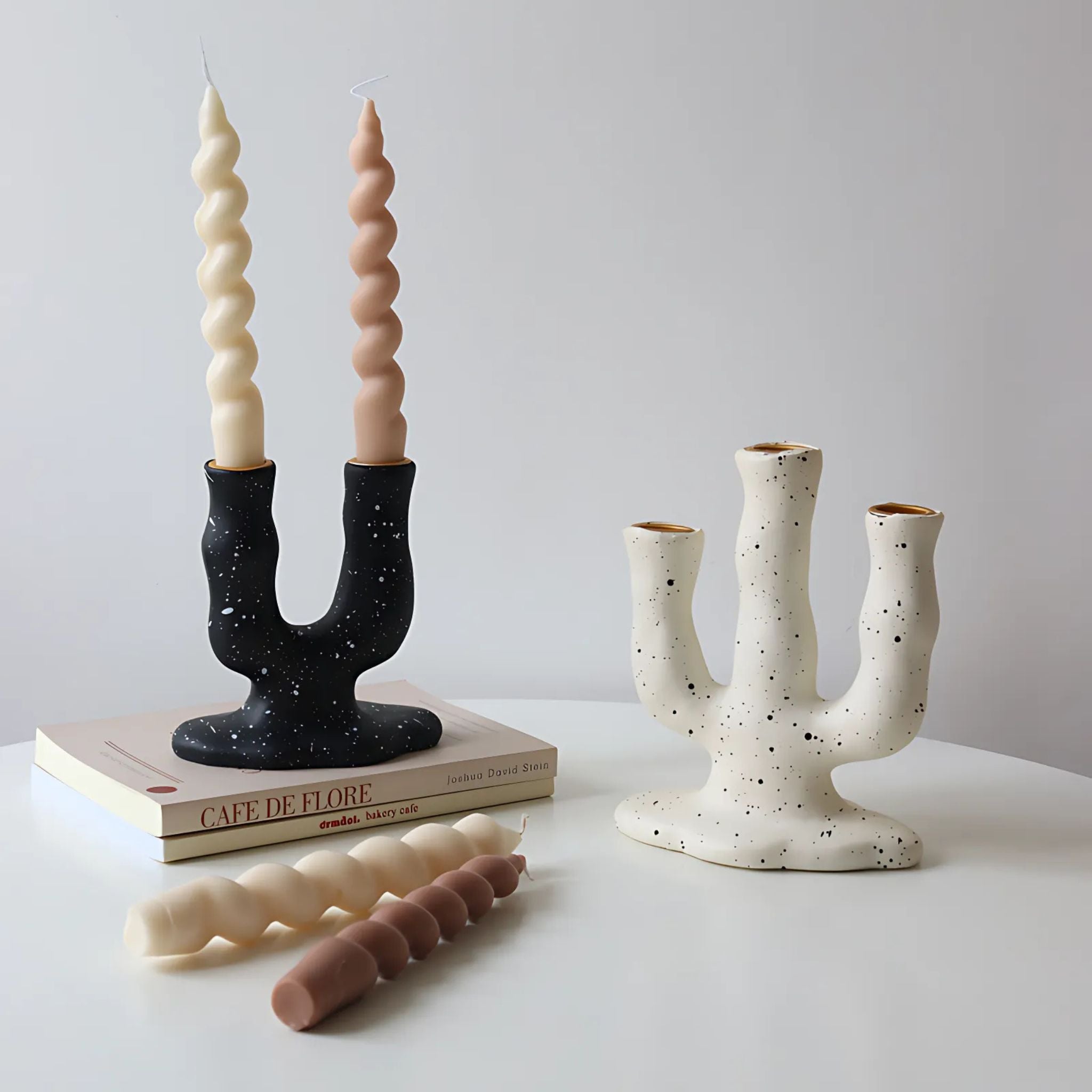 Countertop with decorative ornaments including stacked design books, twisted candles, and two candle holders, one black and one white with arch shape design for multiple candles.