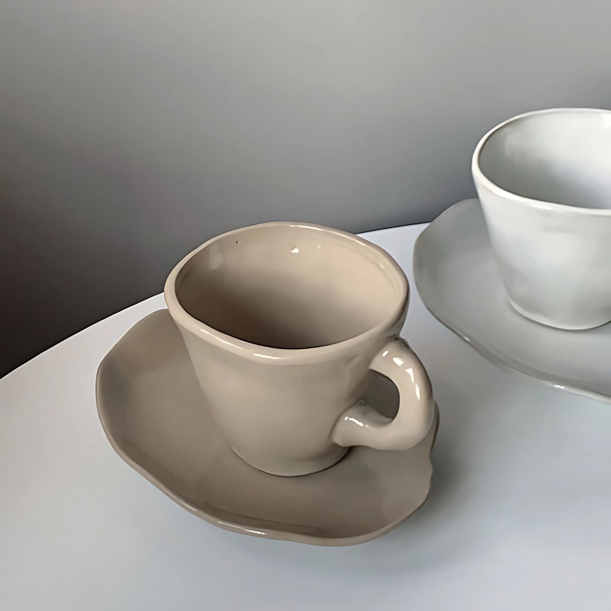 Irregular beige ceramic coffee mug with saucer.