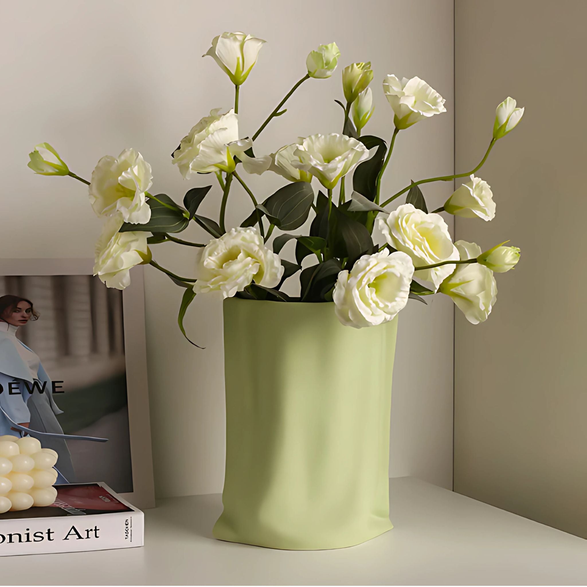 Pastel green ceramic vase on table top with white roses.