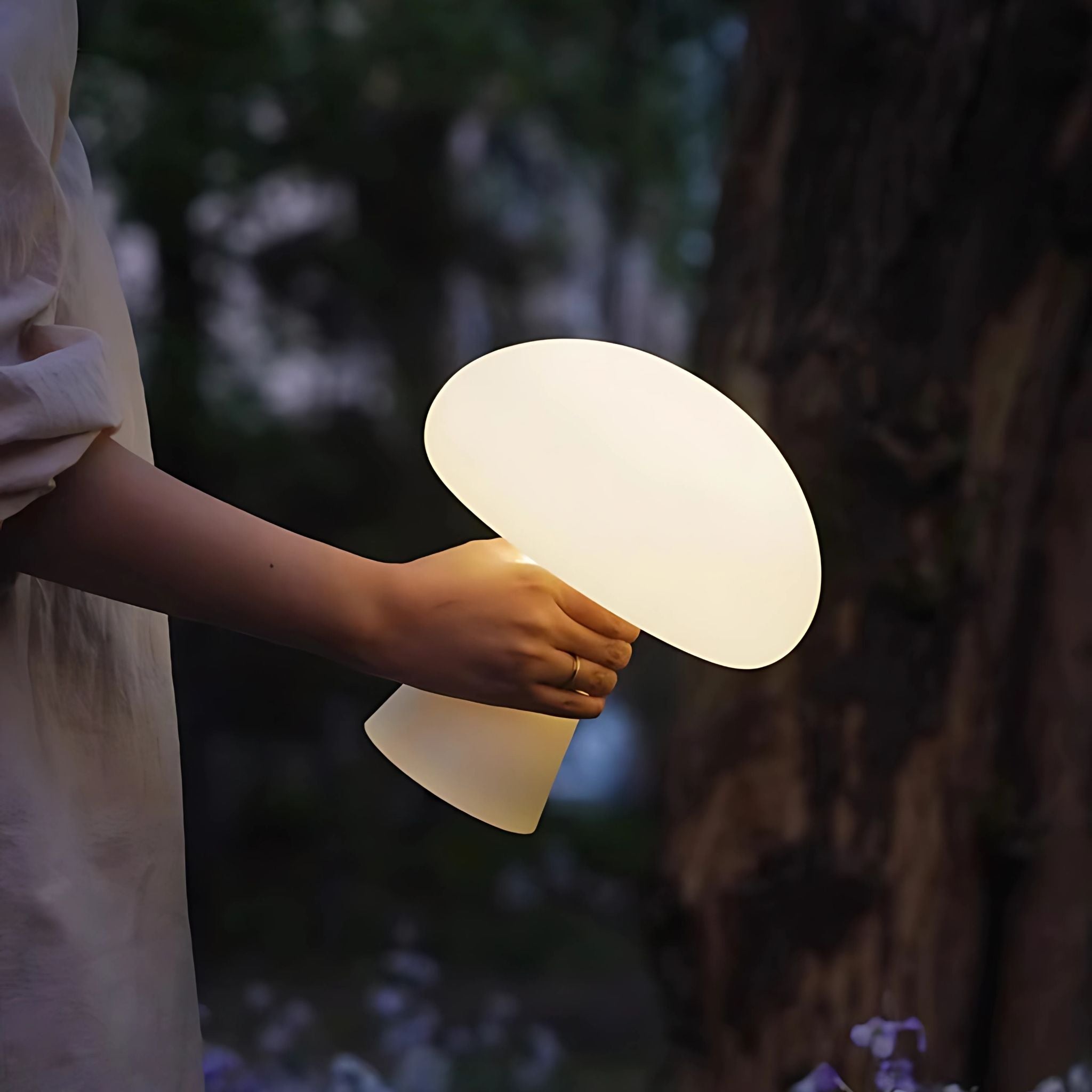 Person holding a white, glowing, mushroom cordless lamp