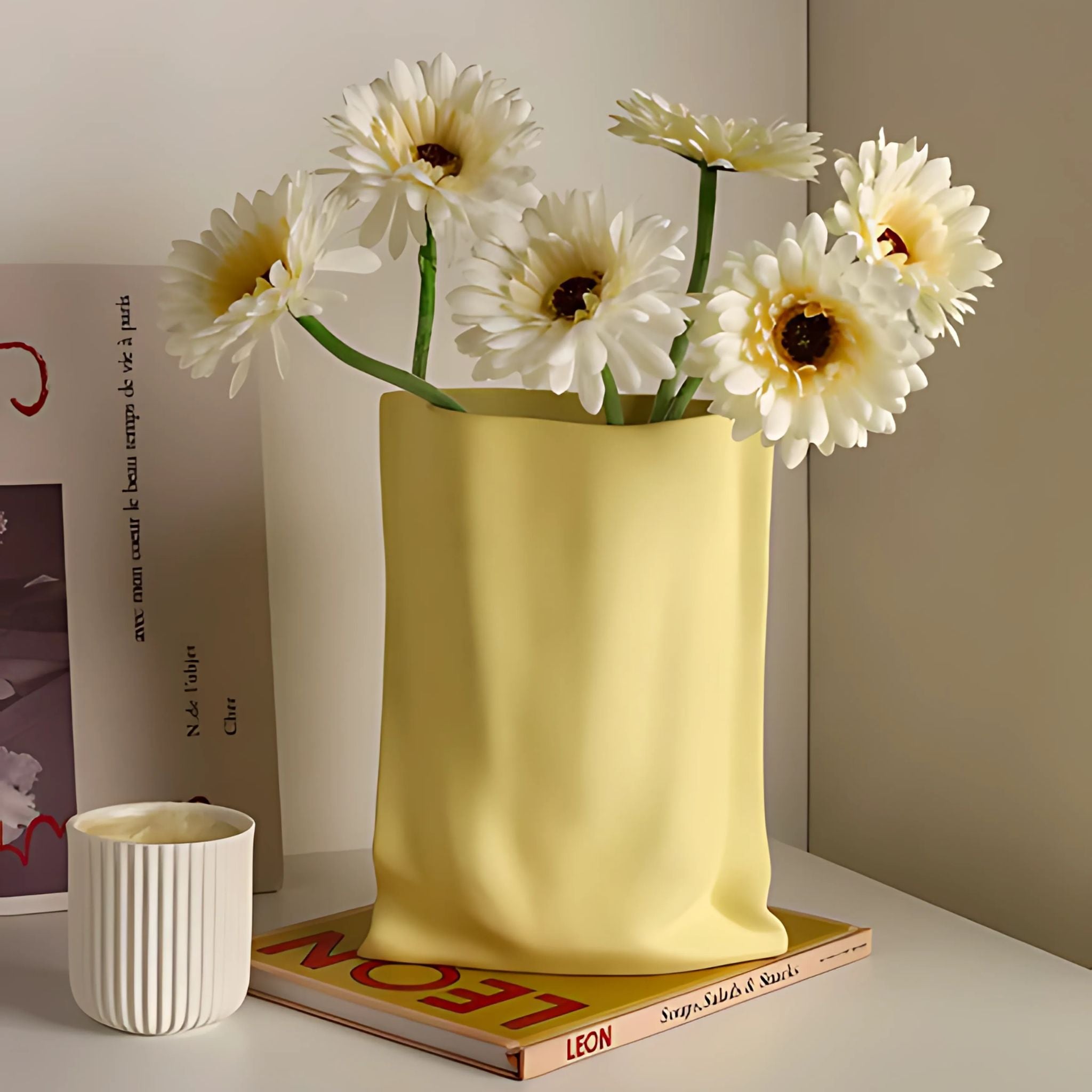 Pastel yellow ceramic bag vase with summer flowers on tabletop.