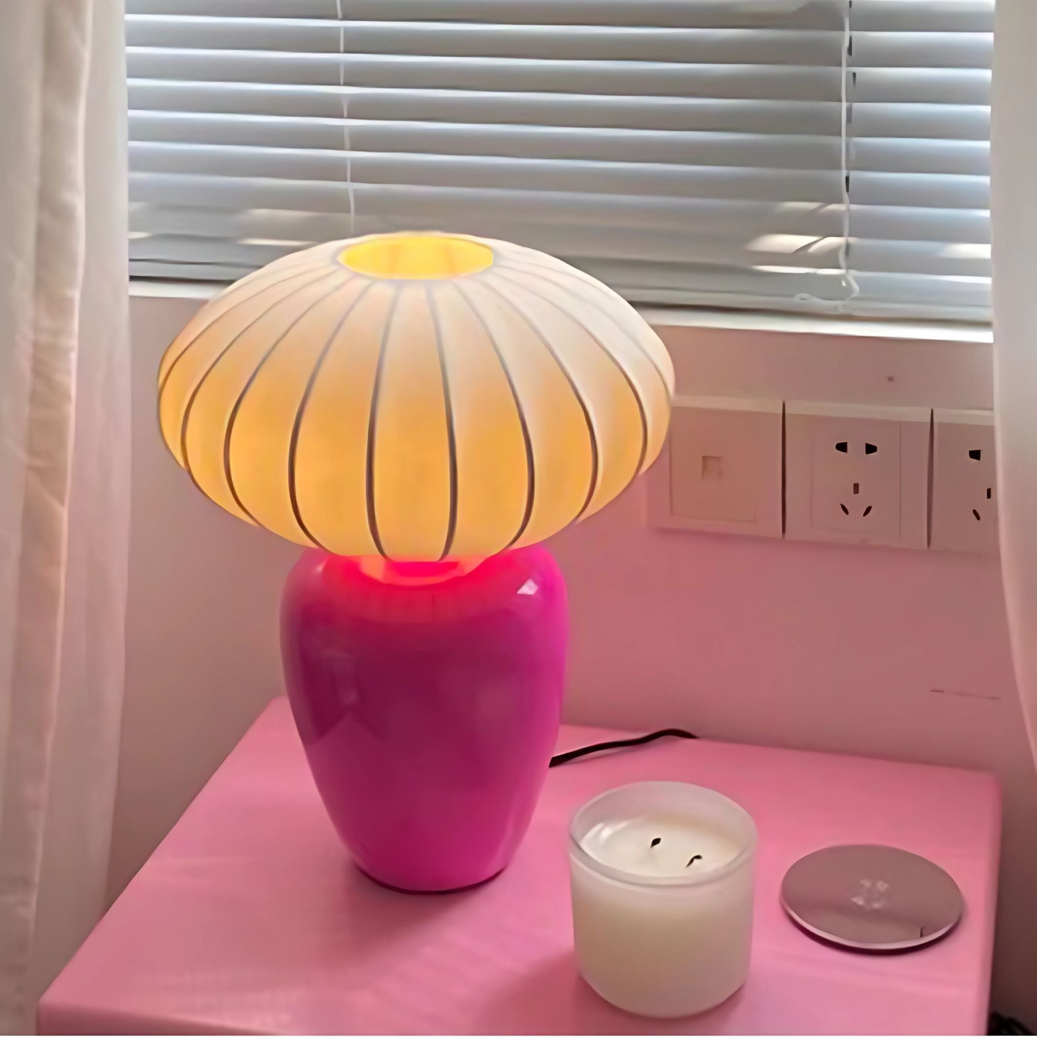 Pink, decorative table lamp on tabletop next to candle.