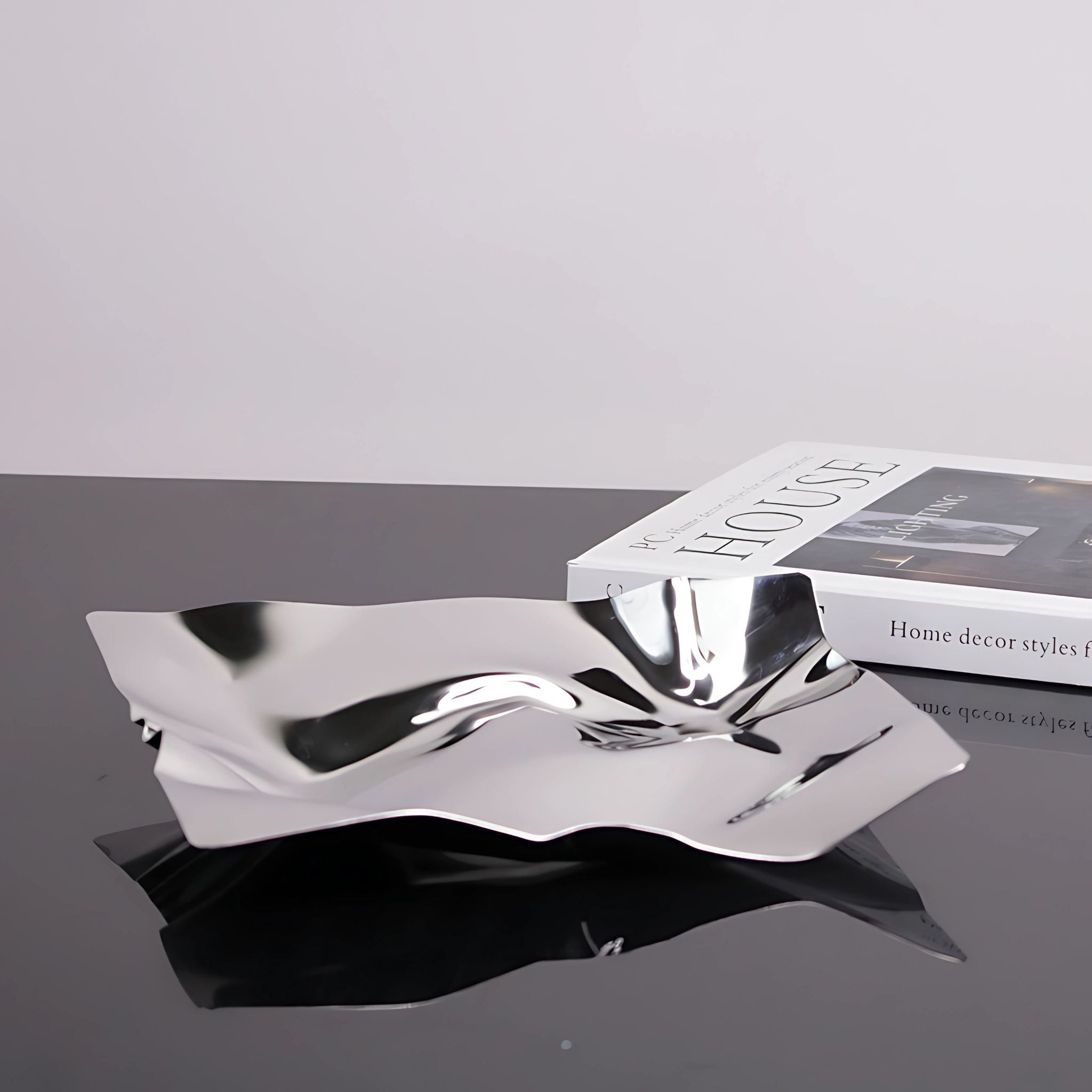 Silver, metallic chrome tray with square, paper wrap design on top of black table next to book.