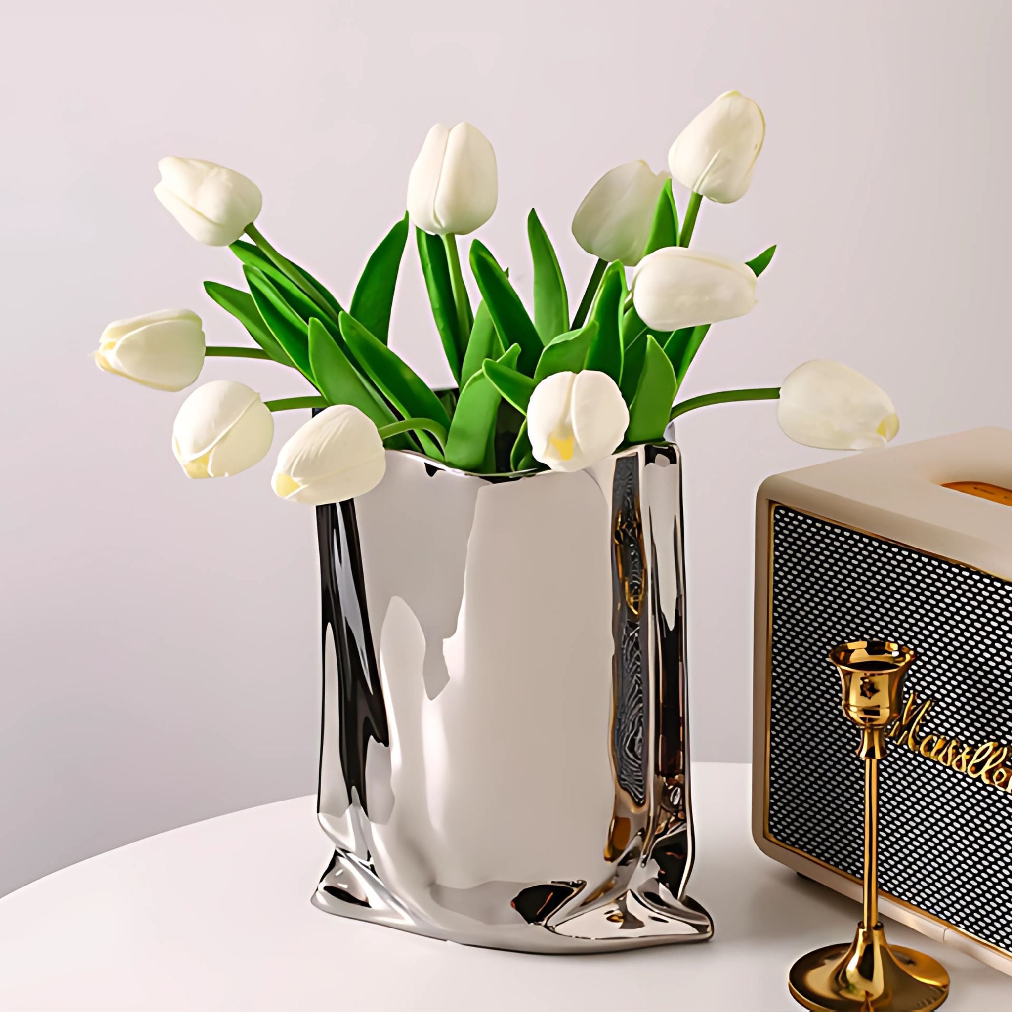Silver electroplated chrome vase with ceramic bag design on tabletop holding white tulips.