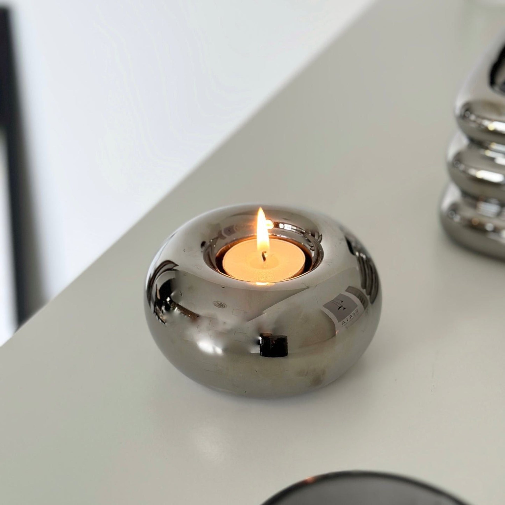 Round, spherical, electroplated silver candleholder with flamed candle.