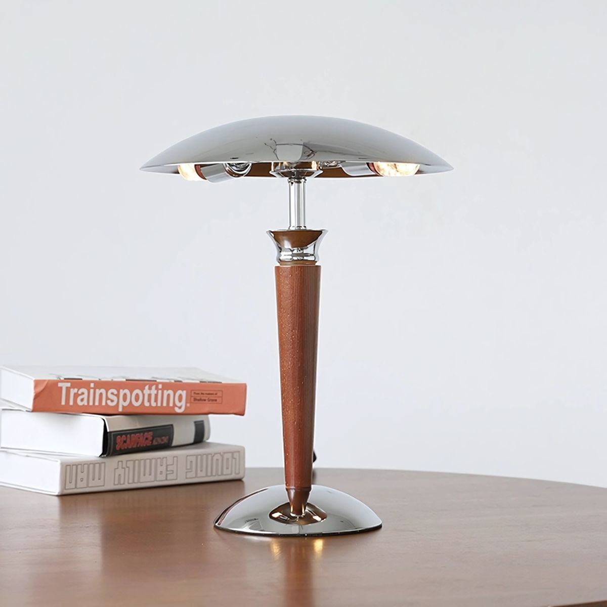 Table lamp with wooden pole and silver steel base and lamp shade on top of a wooden table with books.