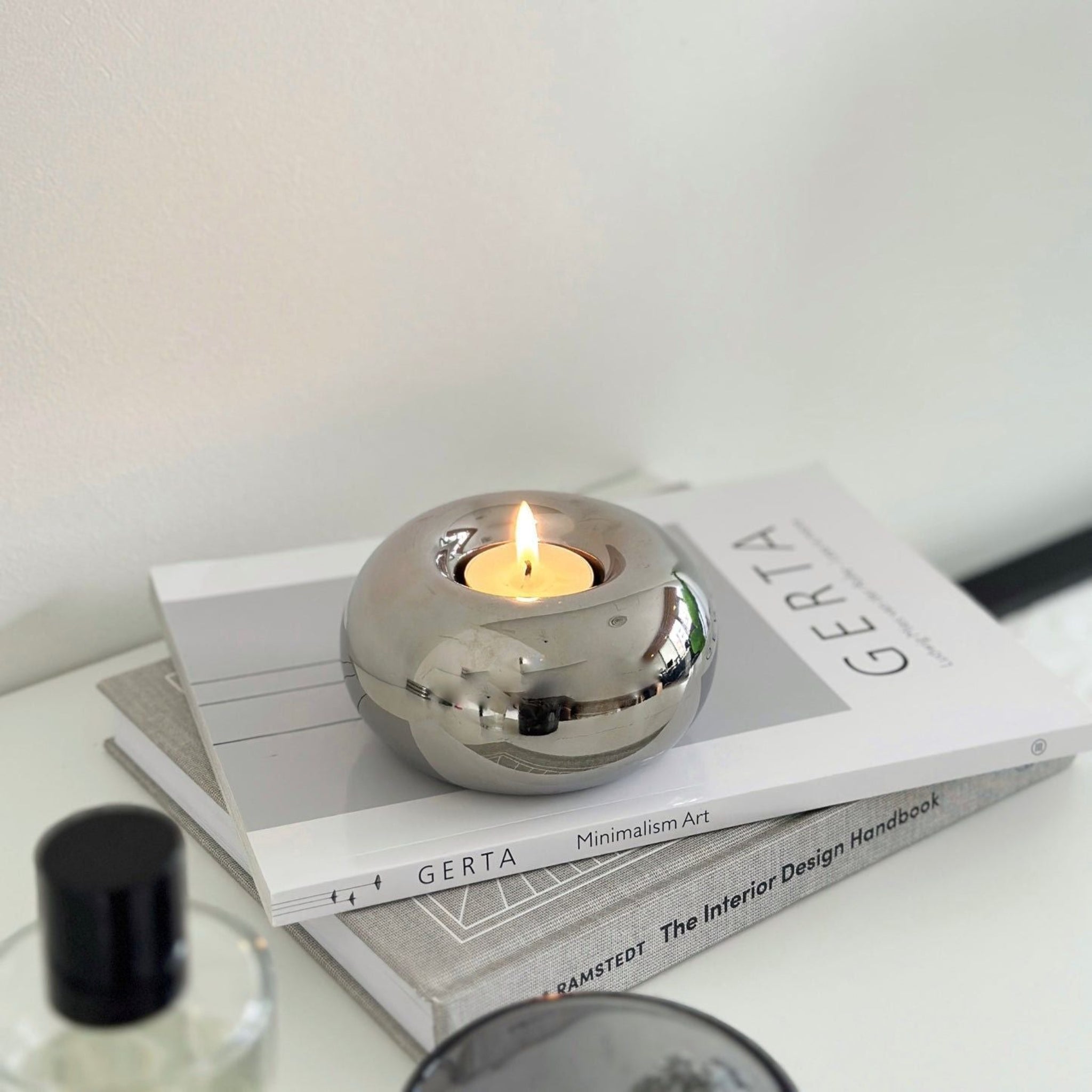 Spherical, silver, round candleholder with candle on top of design books.