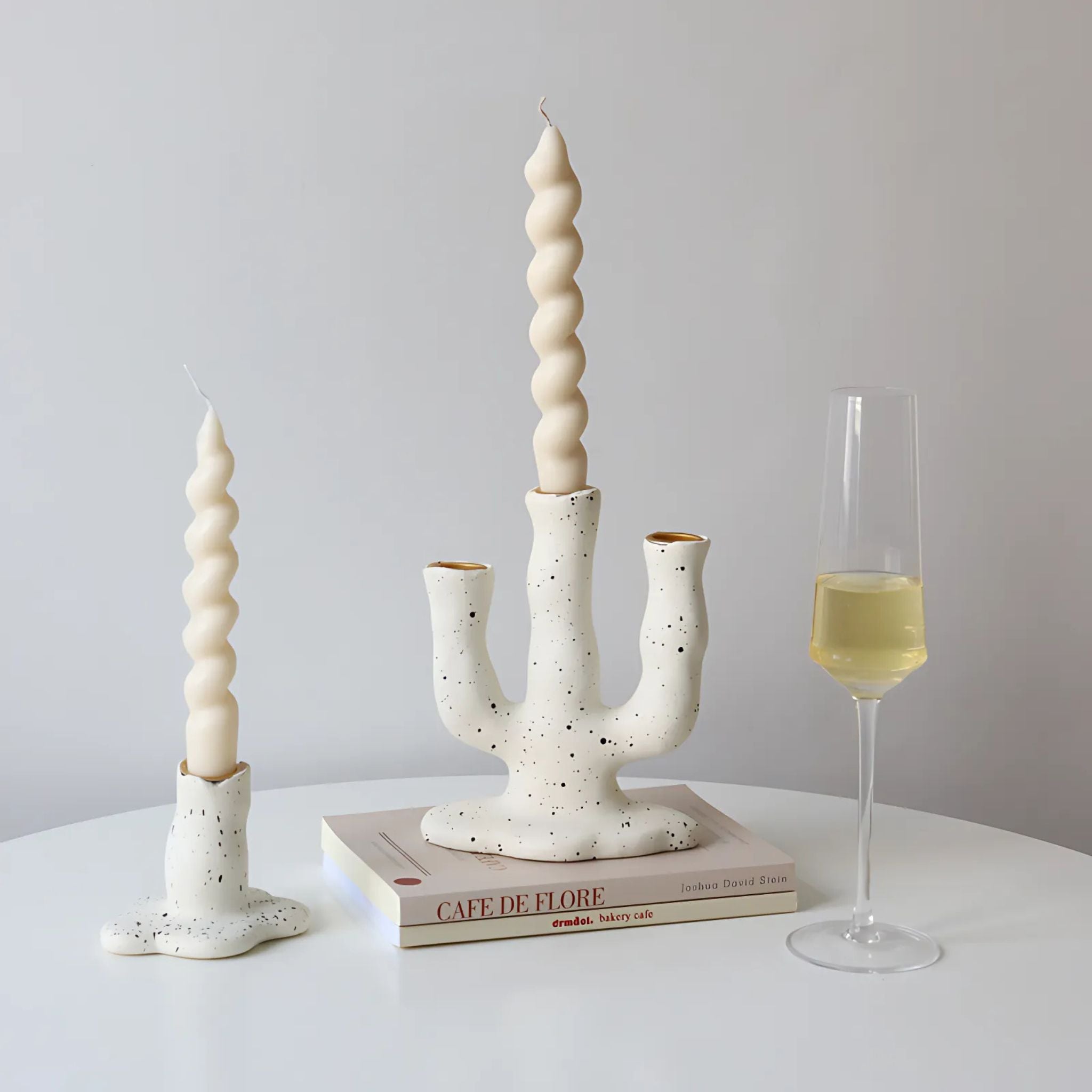 White, arch shaped candlestick holders on counter top with design books and a glass of white wine.