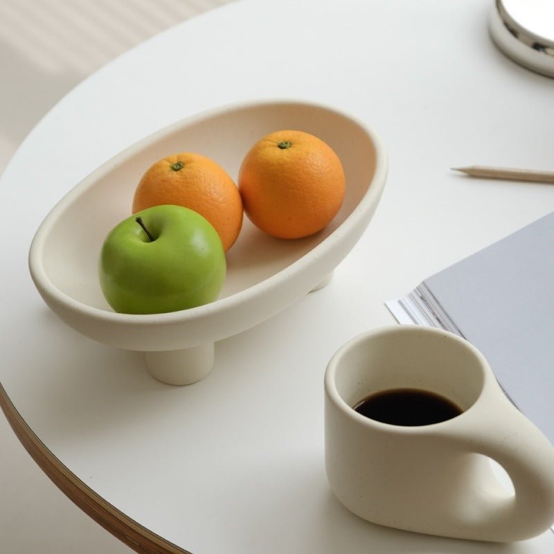 White ceramic elevated fruit bowl and coffee cup on dining table.