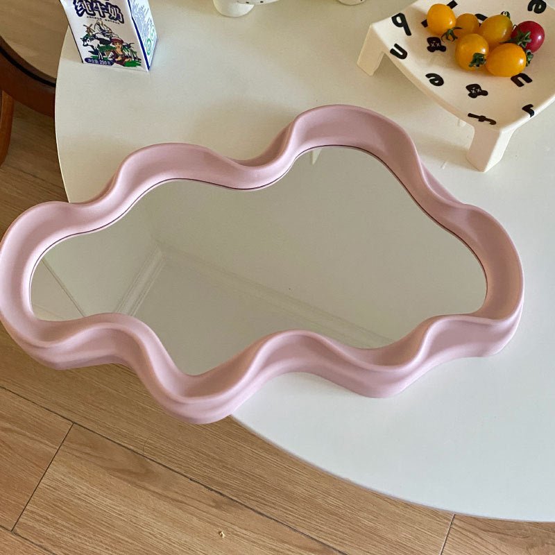 Irregular pink frame mirror on table.