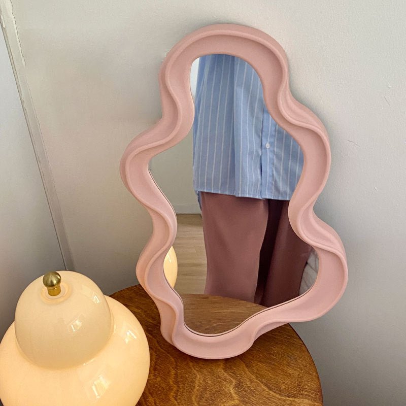 Pink asymmetrical frame mirror on wooden table.