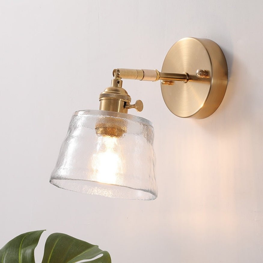 Gold bedside wall lamp with transparent glass shade.