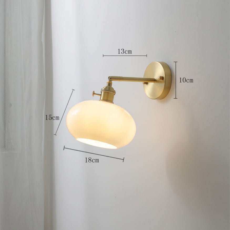Gold bedside wall lamp with white, round glass lamp shade.