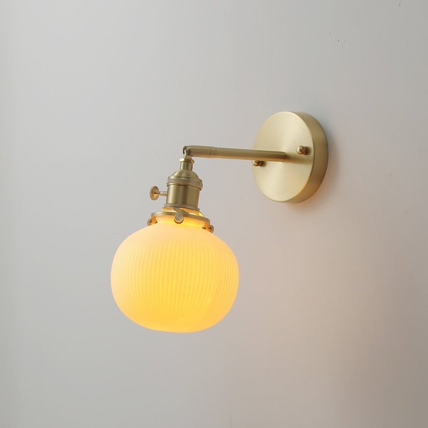 Gold bedside wall lamp with yellow round glass light bulb.