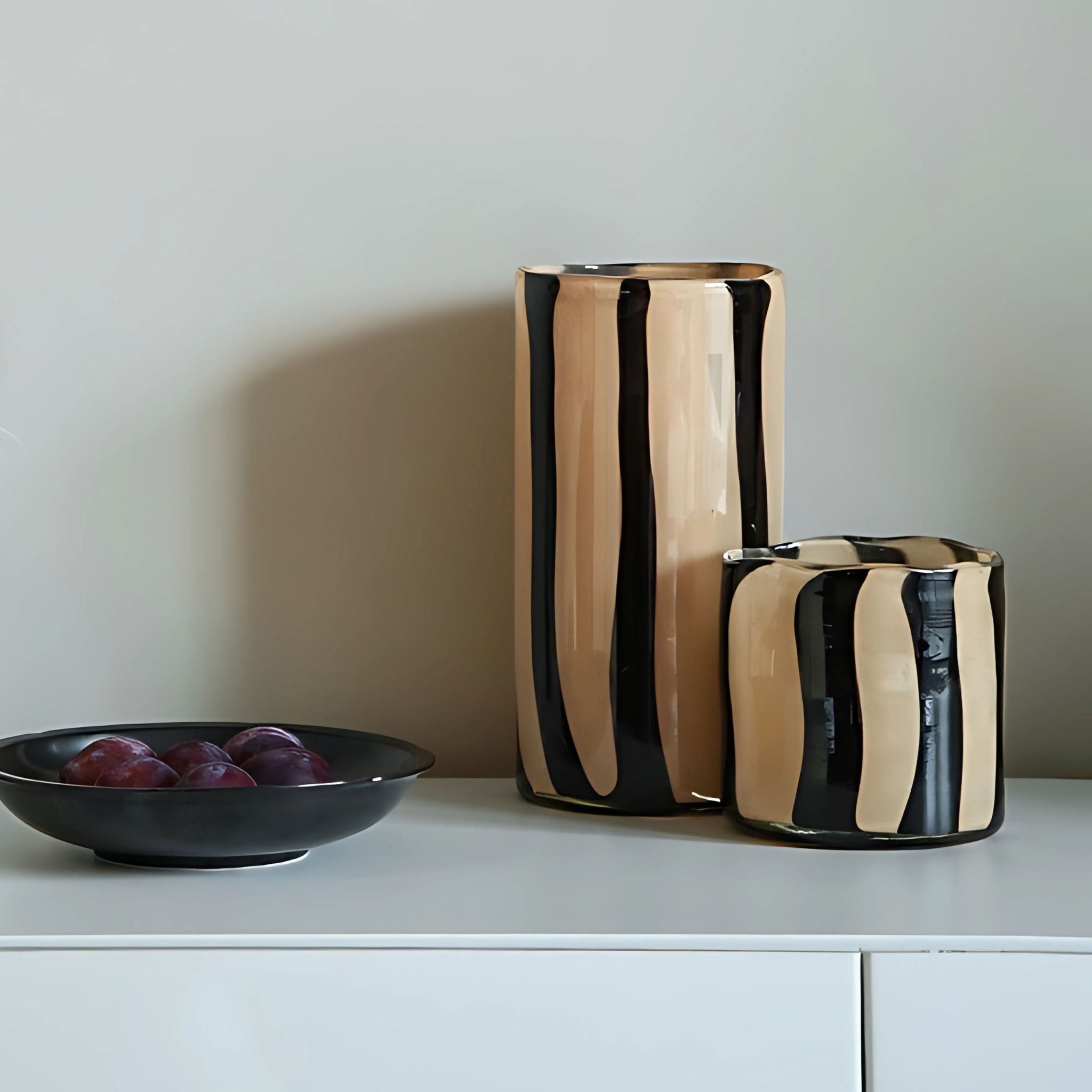 Two glass stripe vases on table top, one tall and one short.
