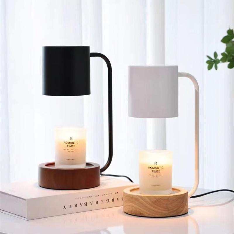 A black and a white metal candle warmer lamps with wooden base, standing on top of a table with candles.