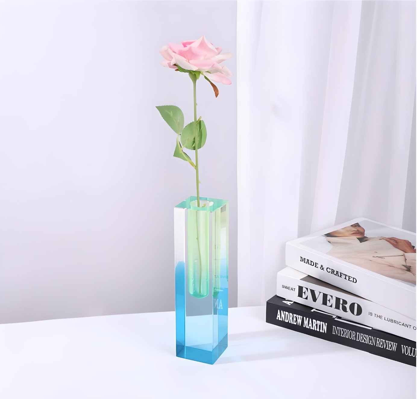 blue and green acrylic vase with pink flower on table.