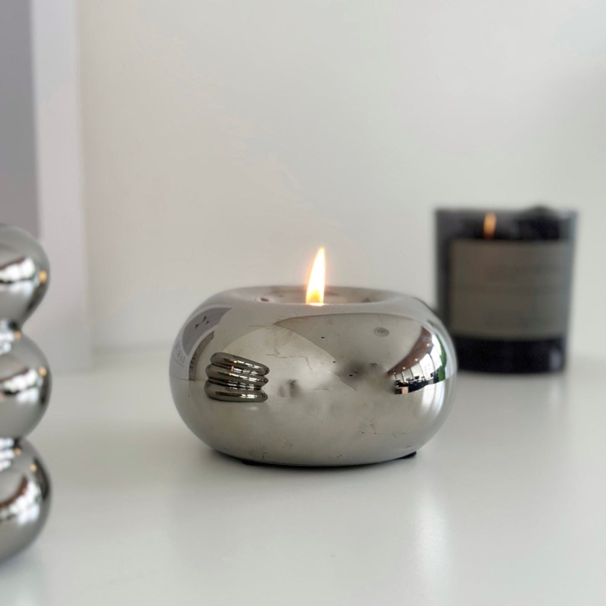 A Chrome, spherical ball candleholder with candle flame.