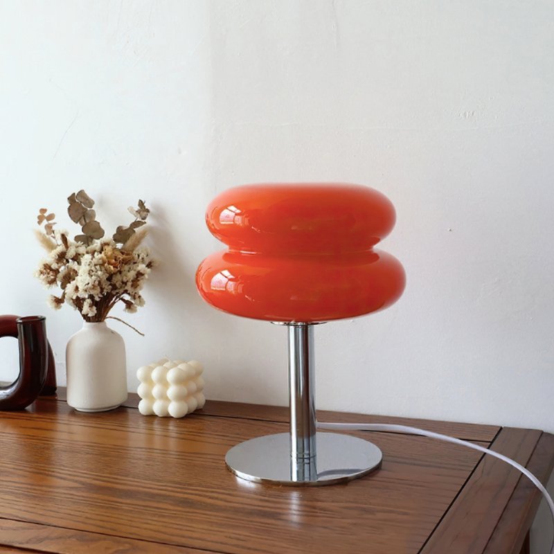 Decorative orange glass lamp with silver brass on wooden table.