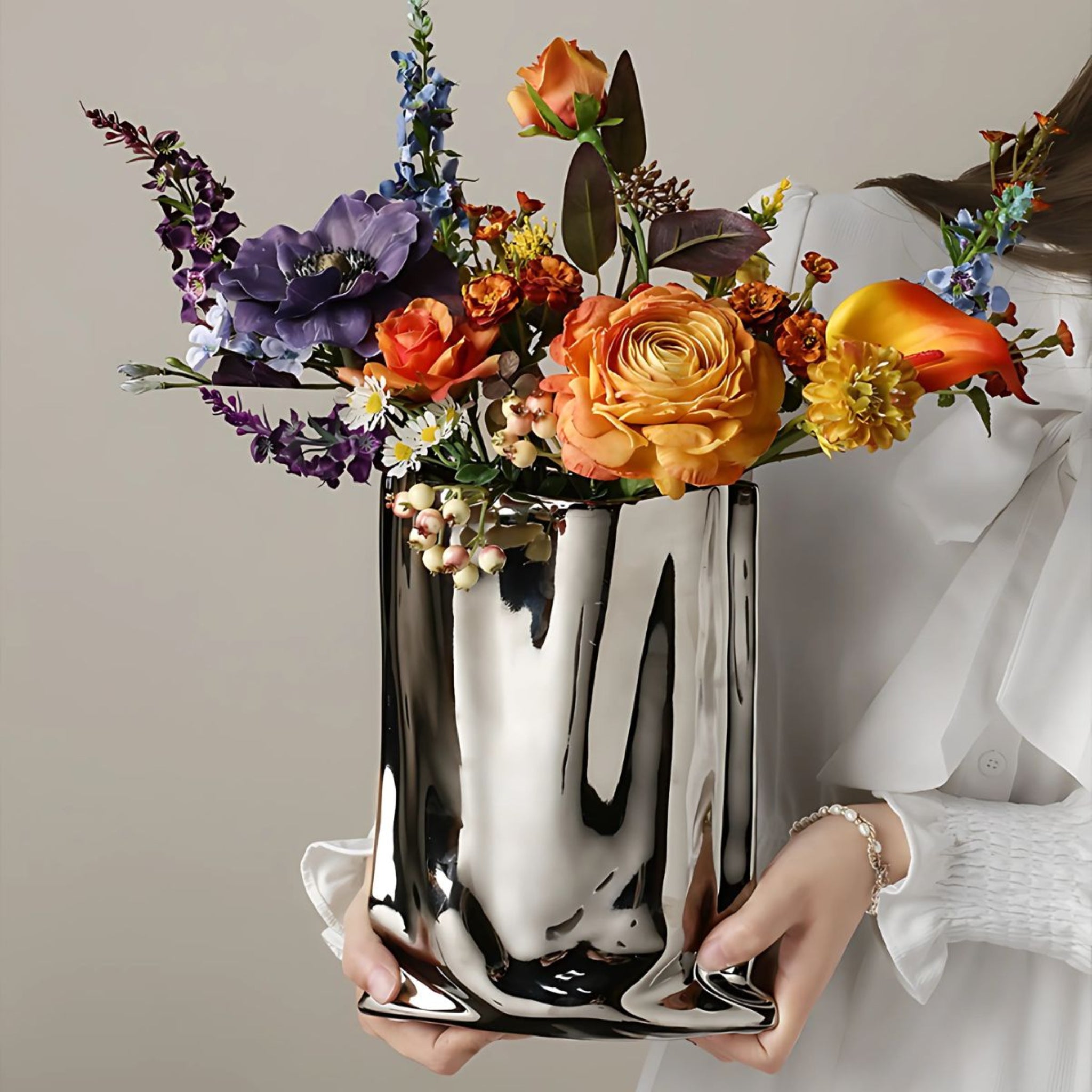 Woman holding an electroplated silver chrome bag vase with a large flower bouquet in orange and purple.