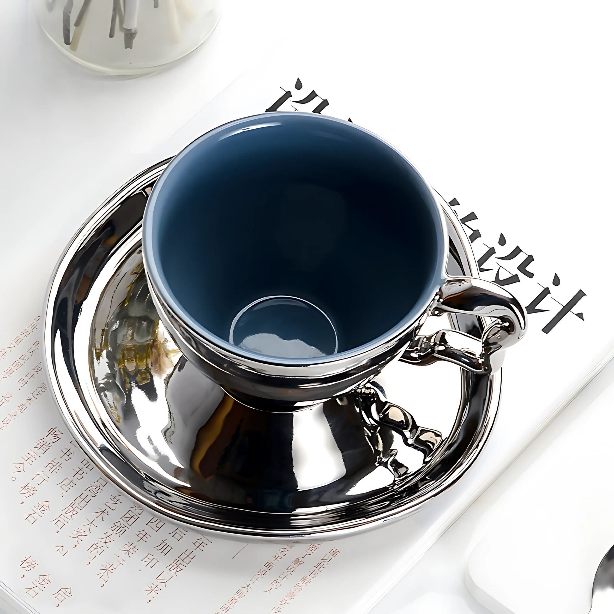 Silver, ceramic tea set with electroplated silver cup and blue on the inside with a matching saucer.