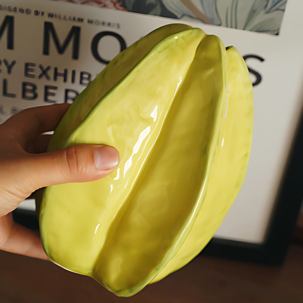 Person holding a yellow, ceramic vase with starfruit design.