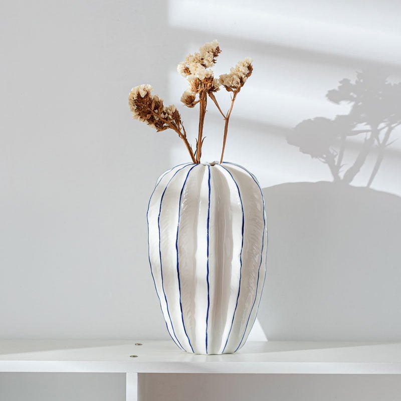 White, ceramic flower vase with blue lines holding dried flowers.