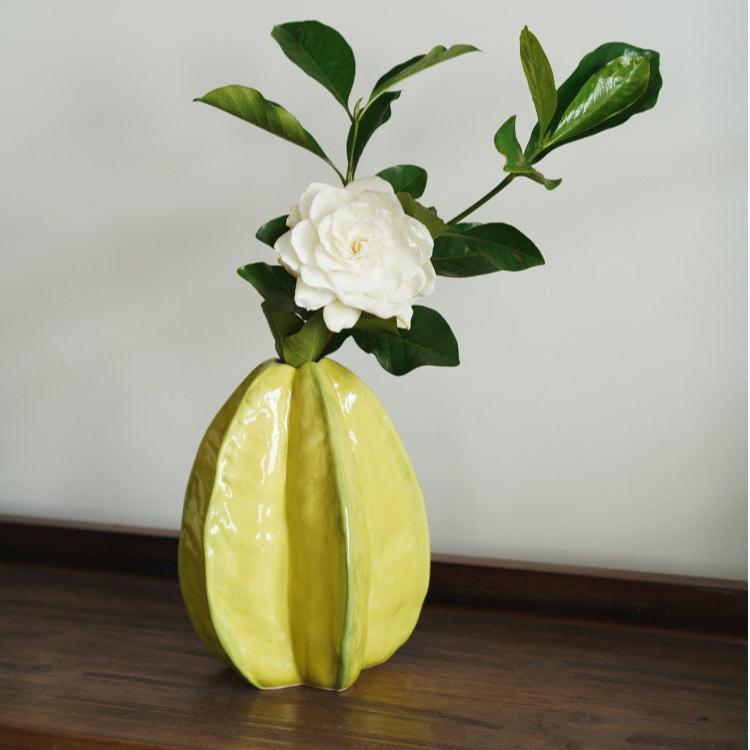 Yellow ceramic vase on top of table with white flower and green branches.