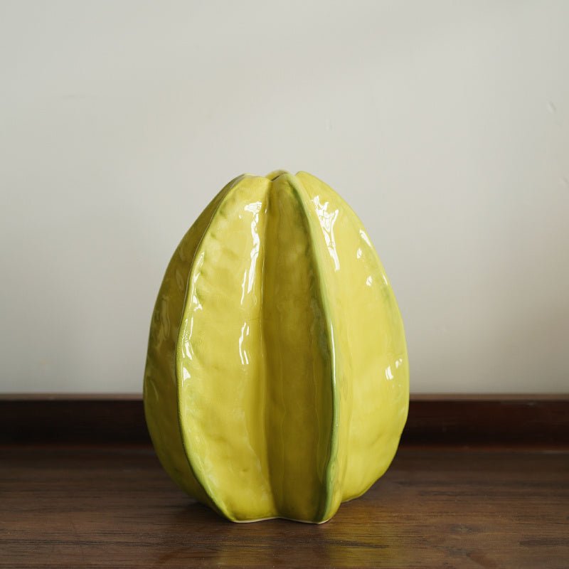 Yellow, ceramic starfruit design vase on table.