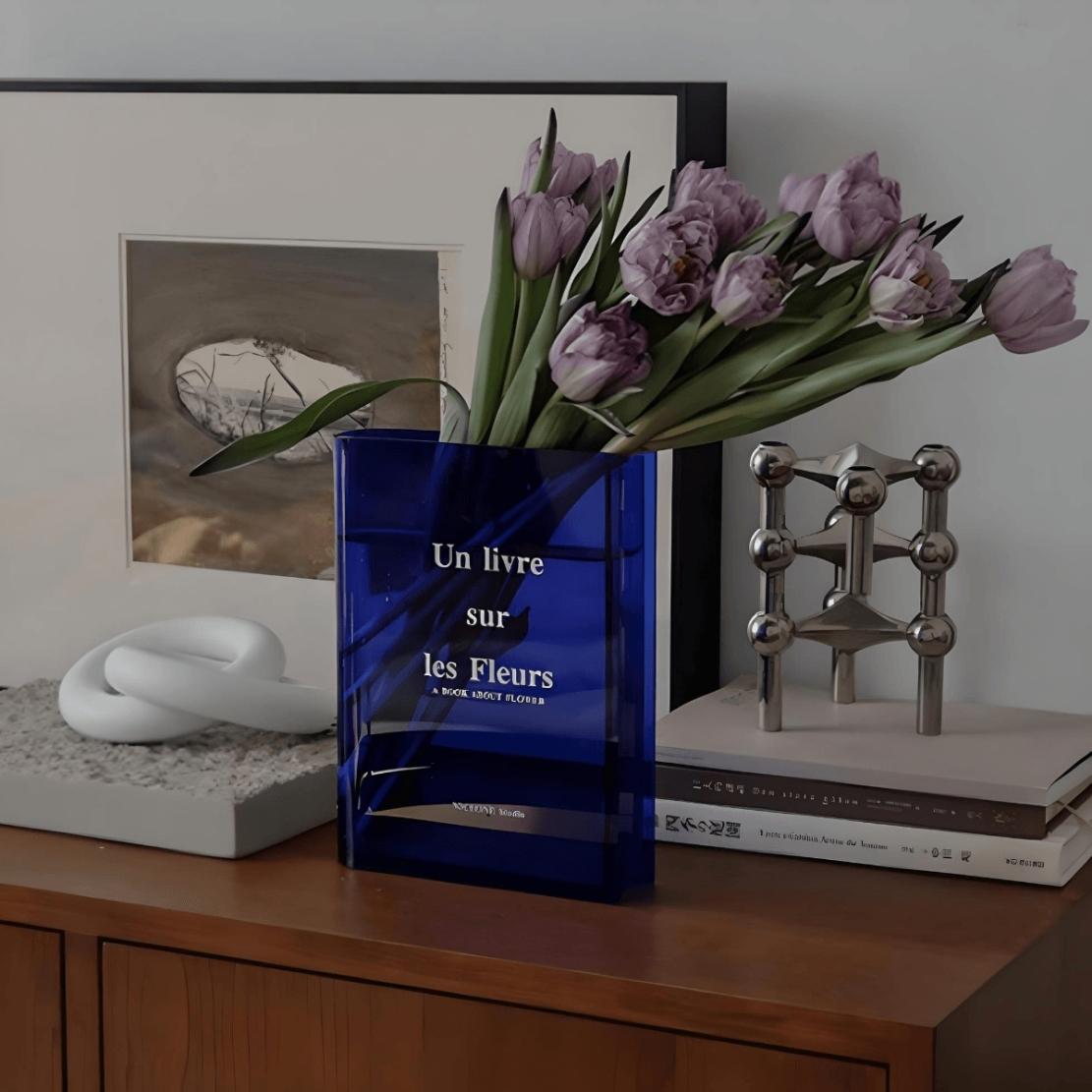 Blue acrylic book vase with text on shelf with purple tulips
