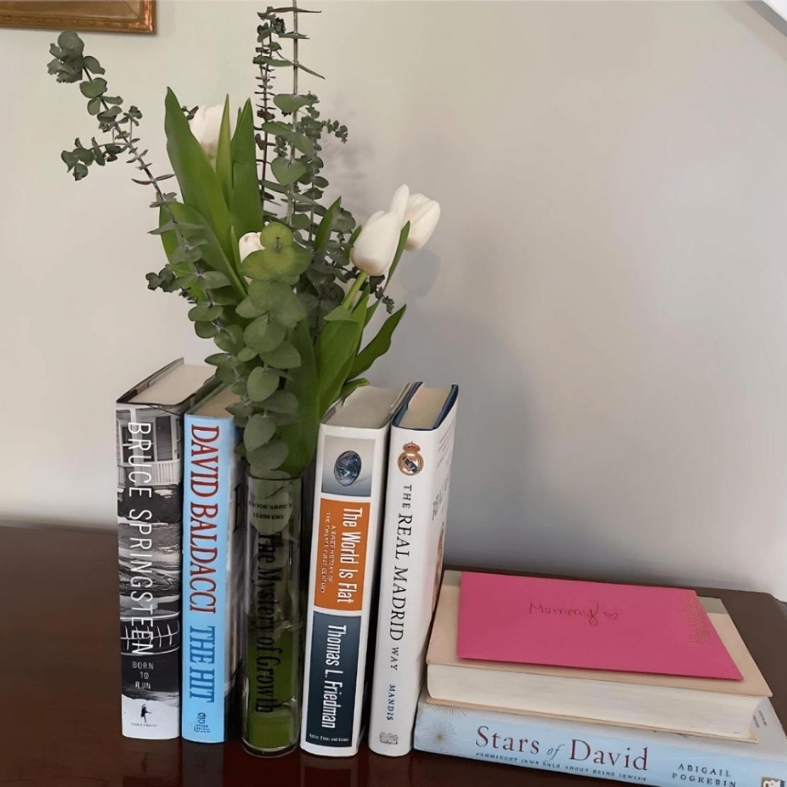 Stacked books and acrylic book vase with text and green flowers