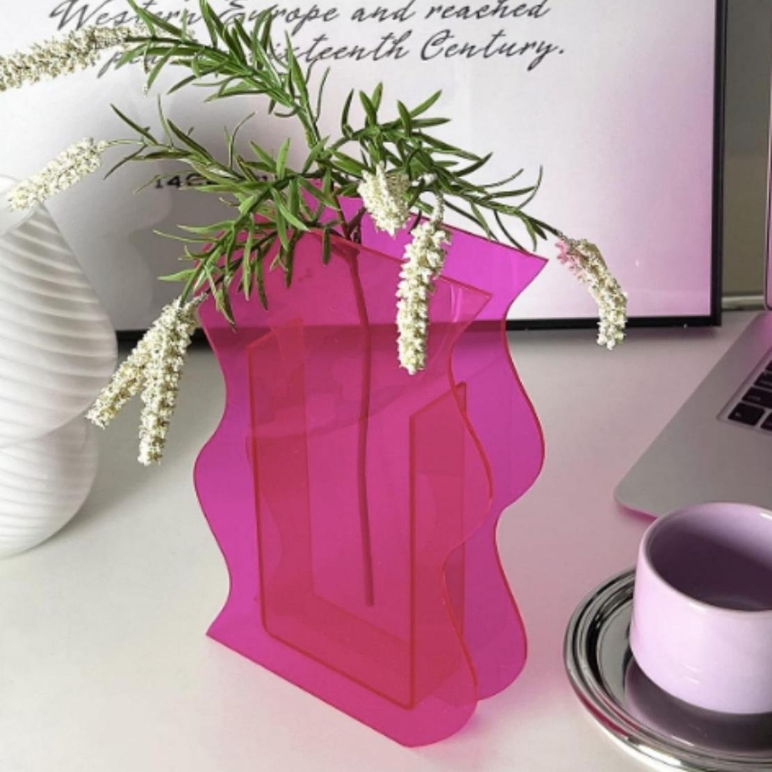 Pink, wavy acrylic vase on table with flowers