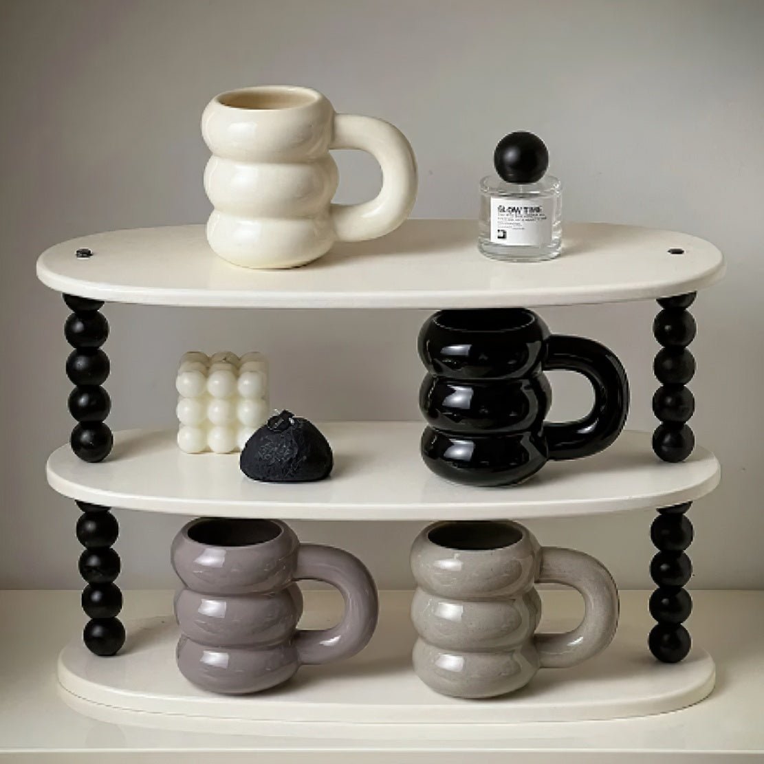 A shelf holding ceramic bubble coffee mugs with a chunky handle in white, black, ashy purple and grey