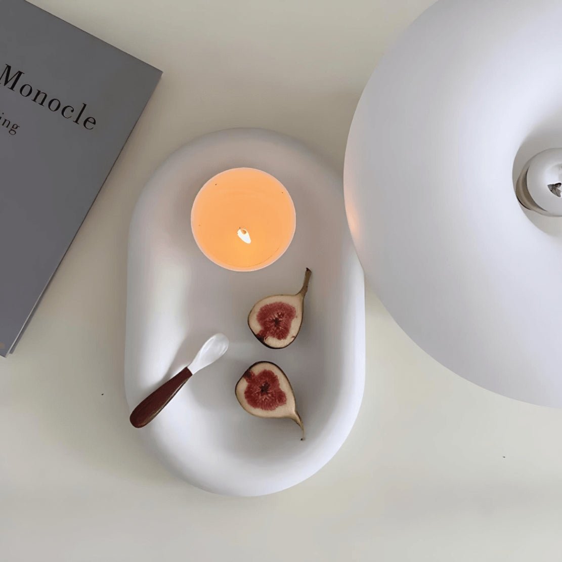 White, ceramic dish with a chunky, oval design, holding a fig and a candle