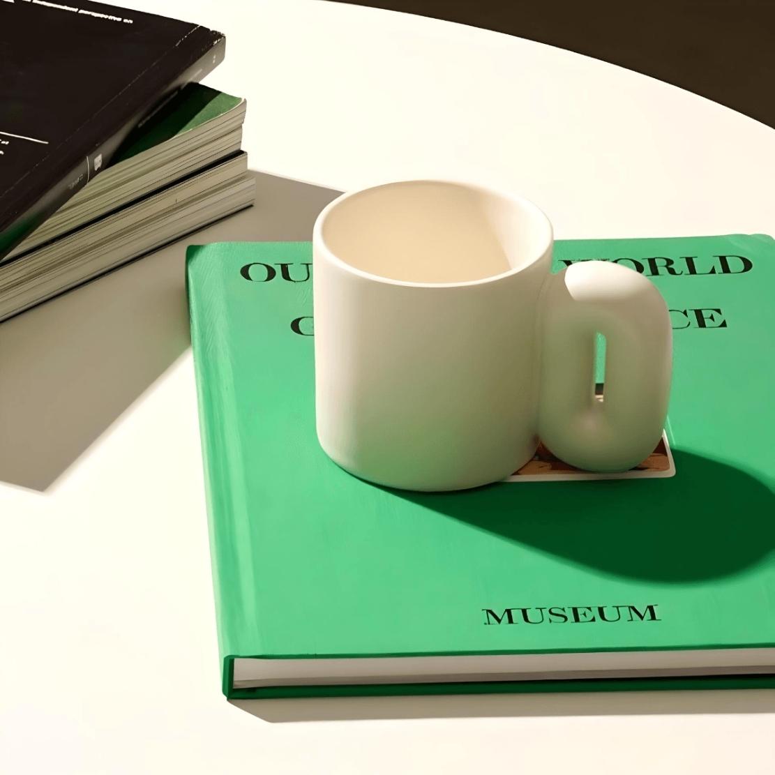 White, ceramic oval shaped handle mug on a green book