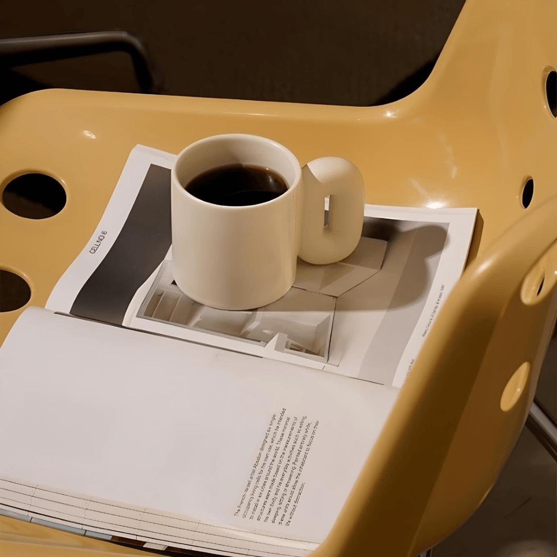 White, ceramic oval handle mug on a magazine and yellow chair