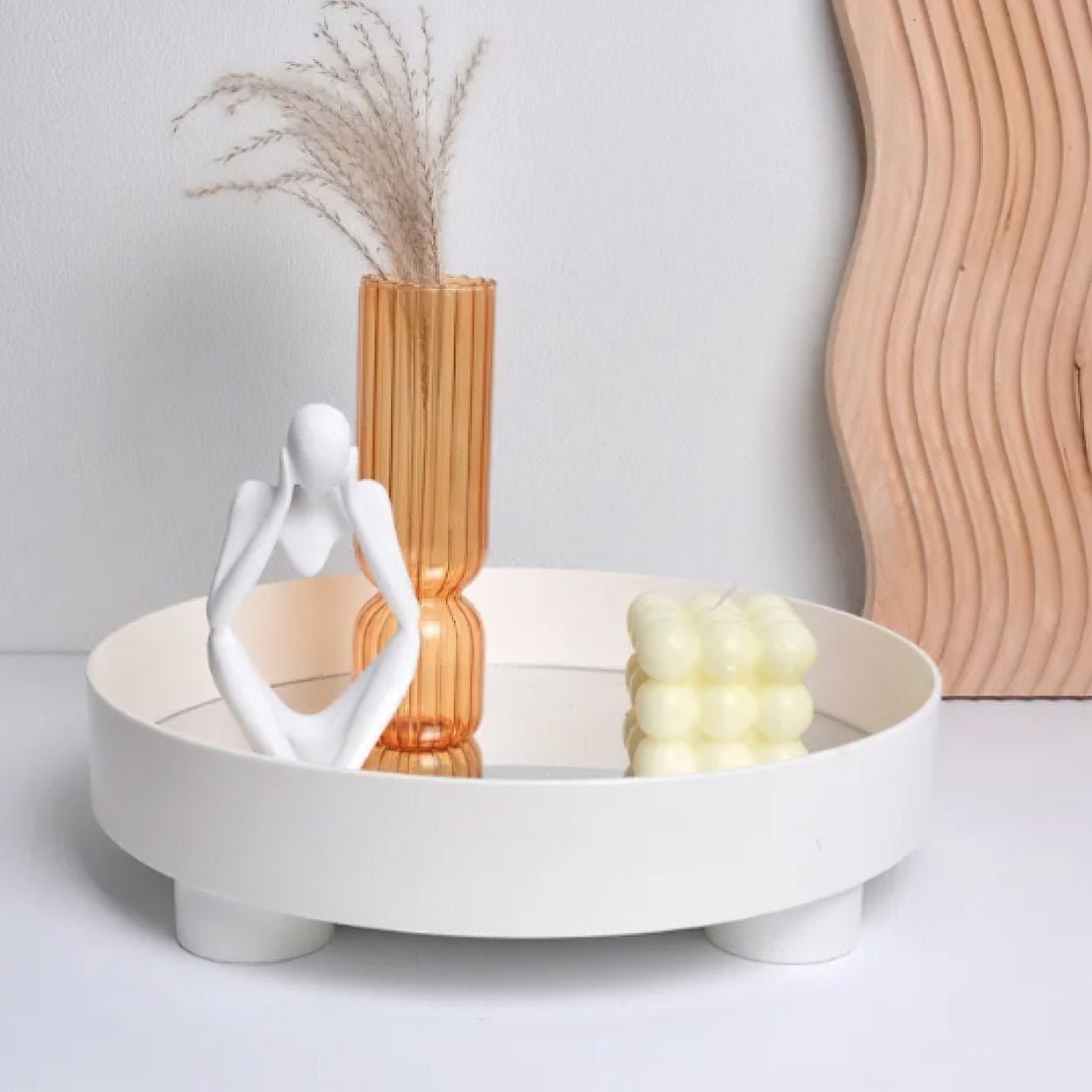 White, round, elevated storage tray, holding a statue, an orange glass flower vase and candle