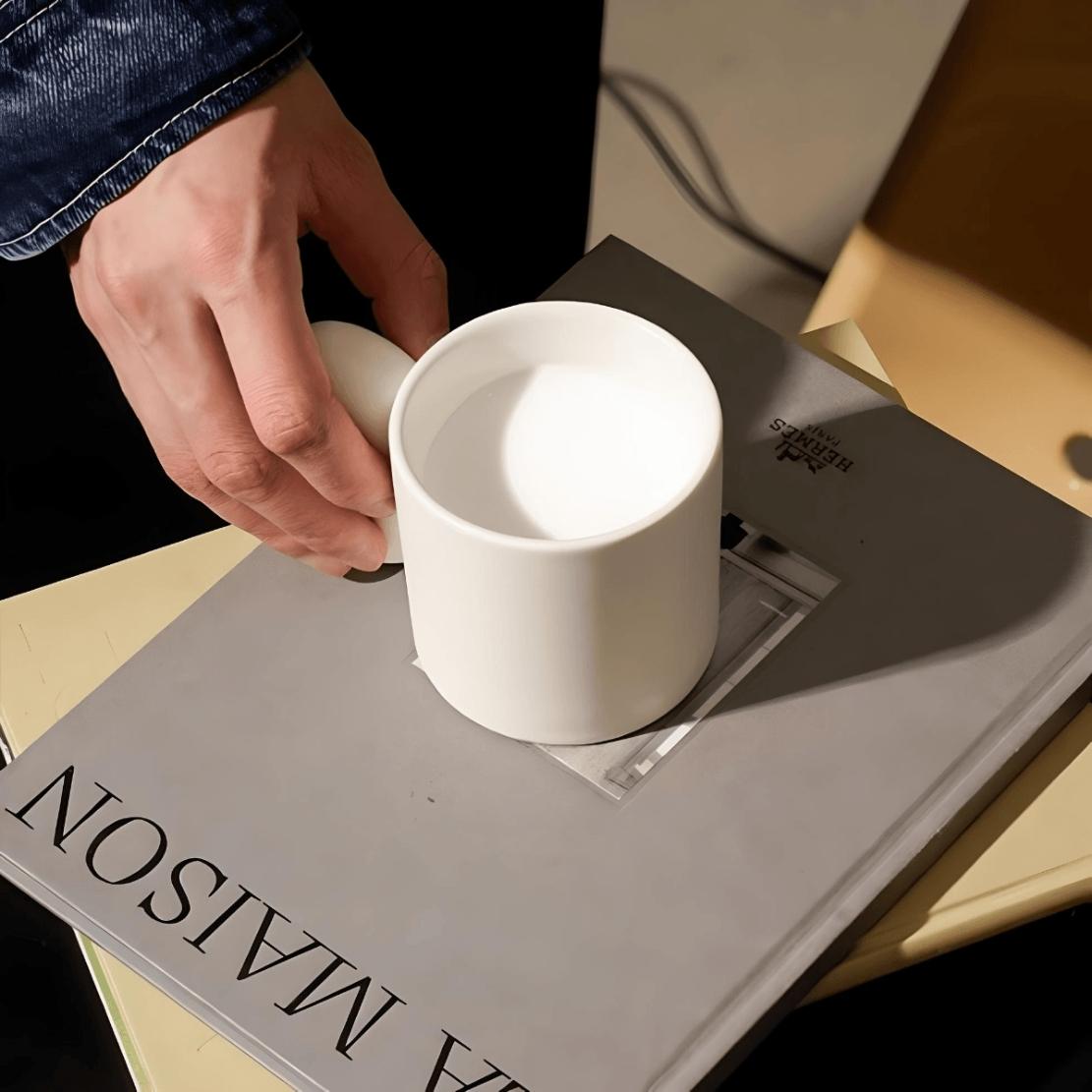 White ceramic oval shape handle mug and grey book