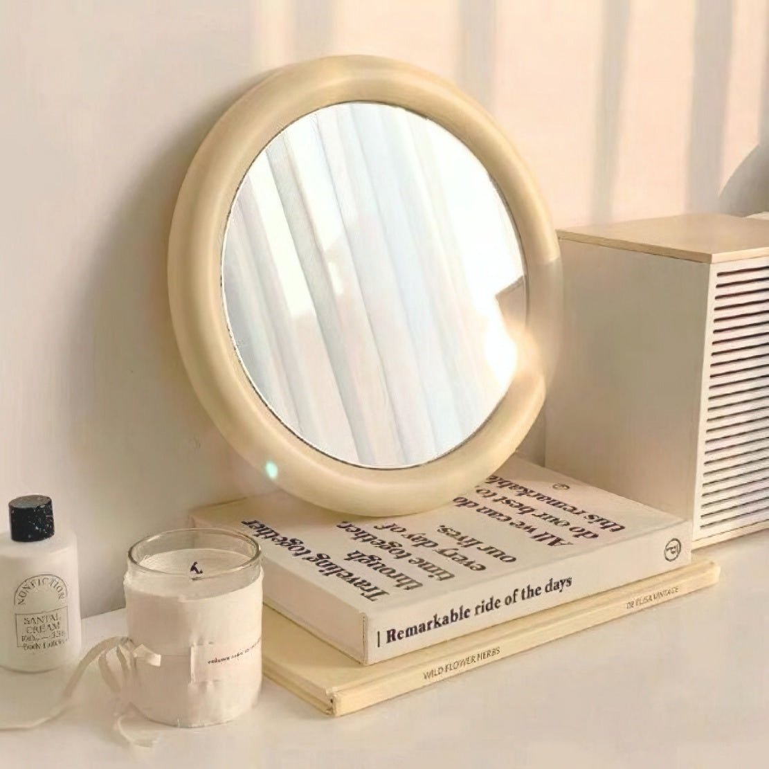 Pastel yellow round frame mirror on tabletop with books and a candle