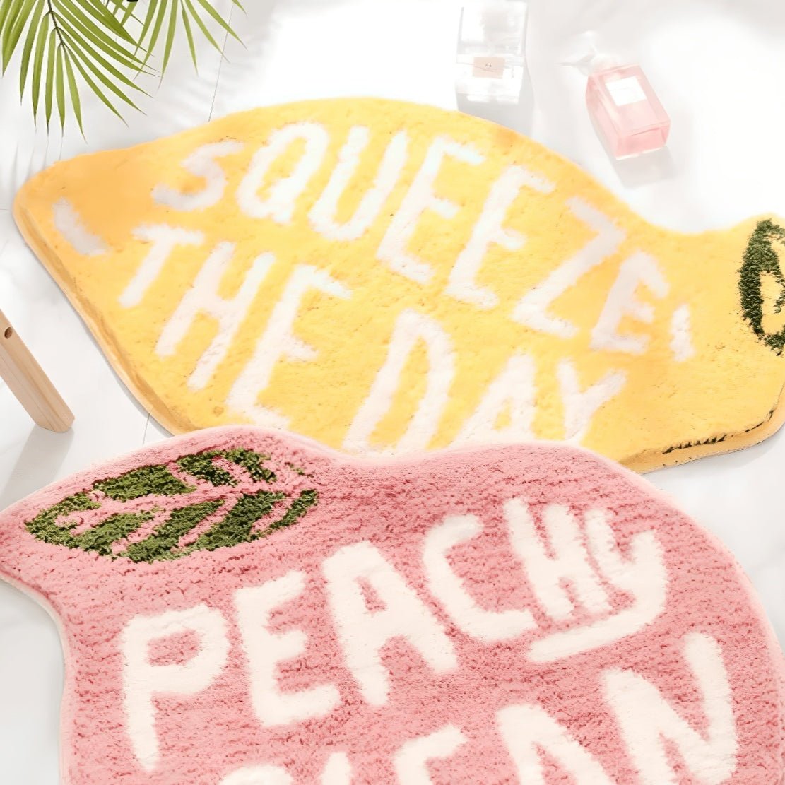 Yellow lemon bathmat with text "Squeeze the Day" and a pink, peach bathmat with text "Peachy Clean"